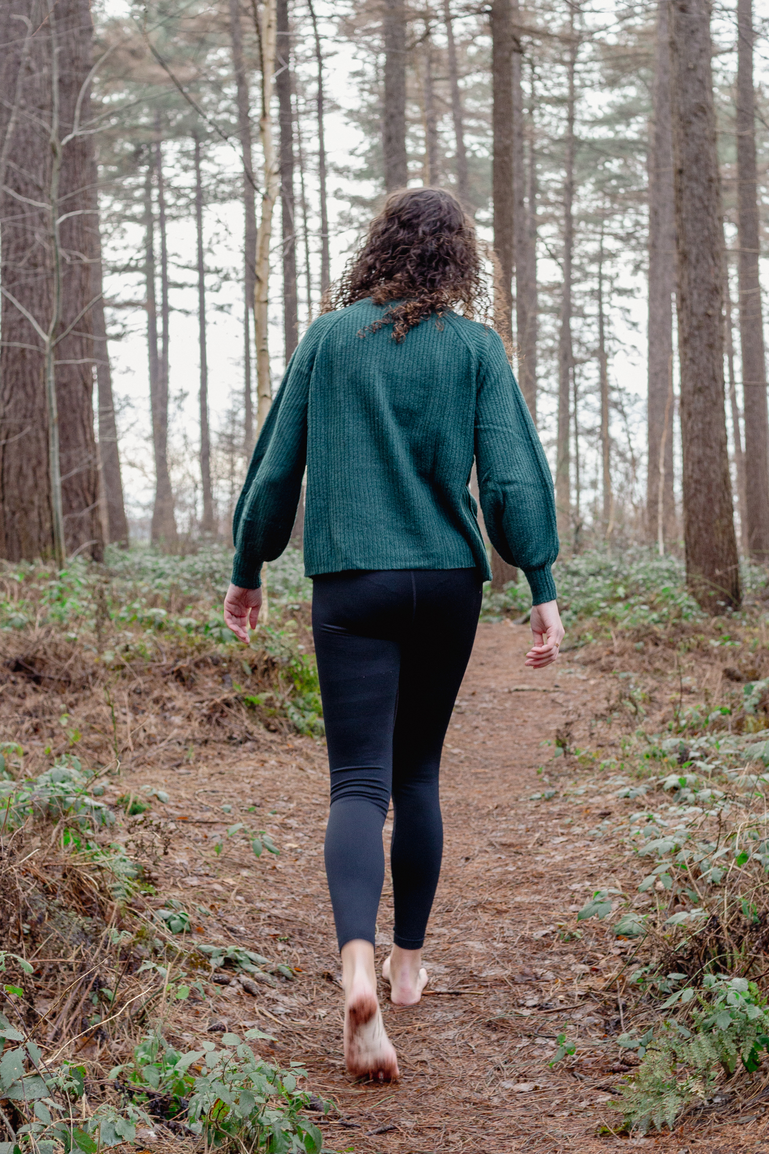 Ik wandel met mijn rug naar de camera in een bosrijk gebied. Ik draag een groene trui.